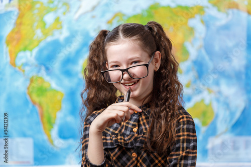 Beautiful teenager girl in glasses on a background of the world map holds a pen in her hands photo