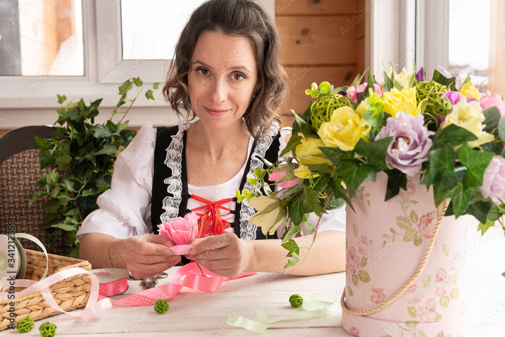 A woman makes a bouquet of flowers from paper on a wooden table