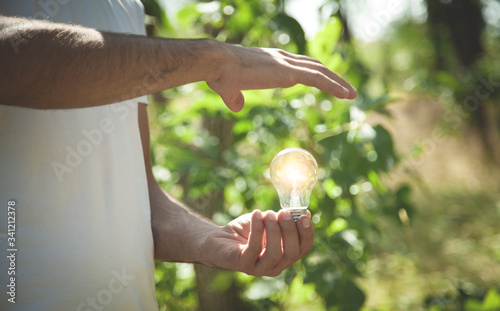 Man holding light bulb in nature. Green energy