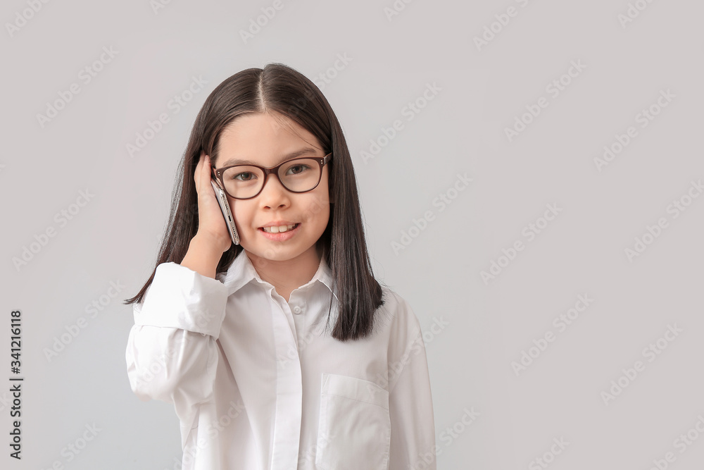 Cute little businesswoman talking by mobile phone on grey background Cute little businesswoman talking by mobile phone on grey background