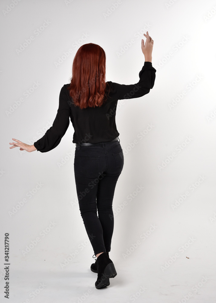 Portrait of a pretty girl with red hair wearing black jeans, boots and a blouse. full length standing pose on a studio background, with back to the camera.
Portrait of a pretty girl with red hair wearing black jeans, boots and a blouse. full length standing pose on a studio background, with back to the camera.
