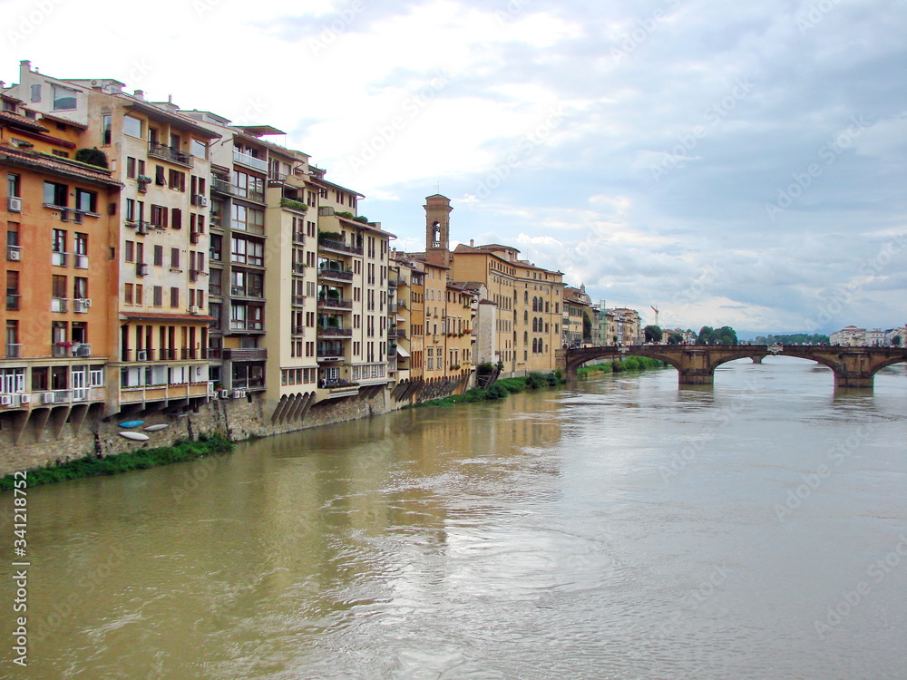 Landscape from the bridge on the Arno River surrounded by ancient Florence houses on a background of cloudy evening sky.