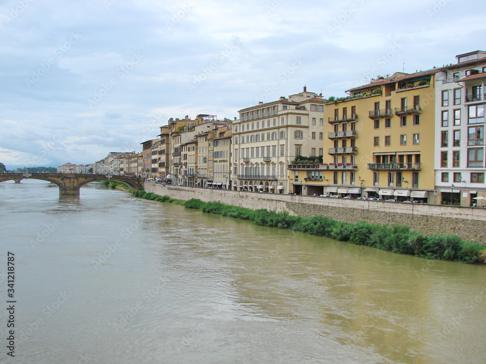 Landscape from the bridge on the Arno River surrounded by ancient Florence houses on a background of cloudy evening sky.