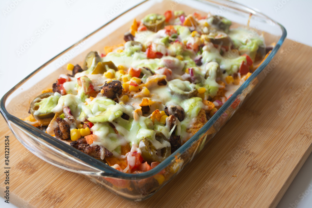 Baked nachos with corn tortilla chips, corn, guacamole, pico de gallo, beans, jalapenos and Monterrey jack in a glass baking dish Baked nachos with corn tortilla chips, corn, guacamole, pico de gallo, beans, jalapenos and Monterrey jack in a glass baking dish
