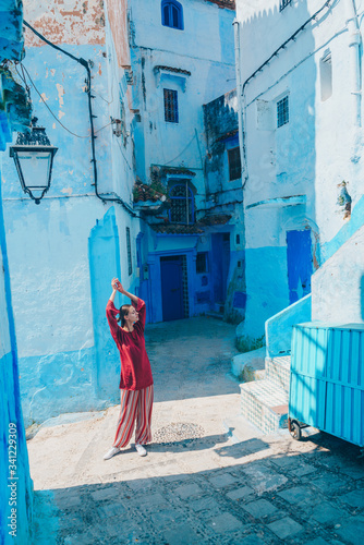 raising hands up a girl in oriental clothes stretches on the streets of the blue city of morocco © nelen.ru
