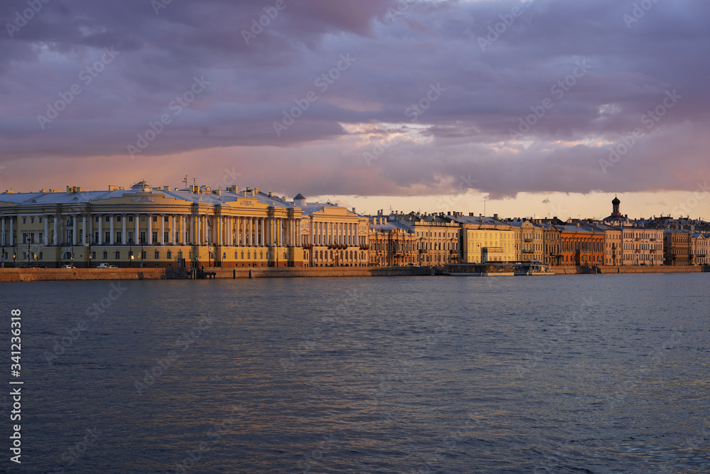 Embankment with a view of the beautiful historical buildings of St. Petersburg in the sunset rays of the sun, beautiful evening sky, the Neva river