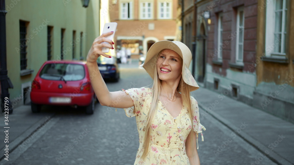 Woman taking selfie on street. Cheerful young woman walking on old European town street and taking selfie with smartphone.