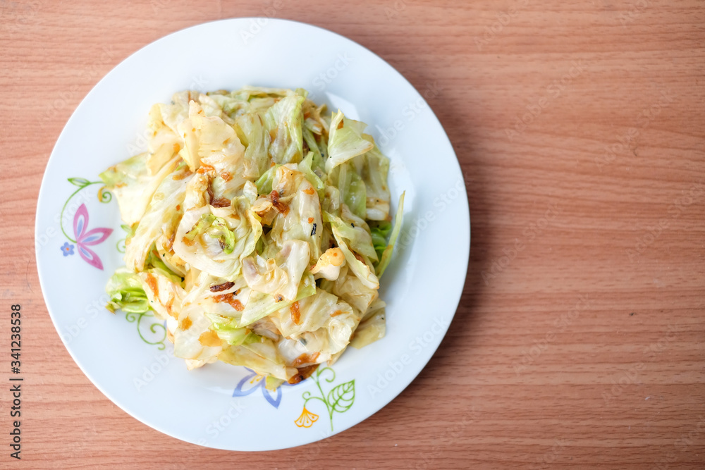 The hot stir fried cabbage with fish sauce serve on white dish set on brown table - homemade food concept. The hot stir fried cabbage with fish sauce serve on white dish set on brown table - homemade food concept.