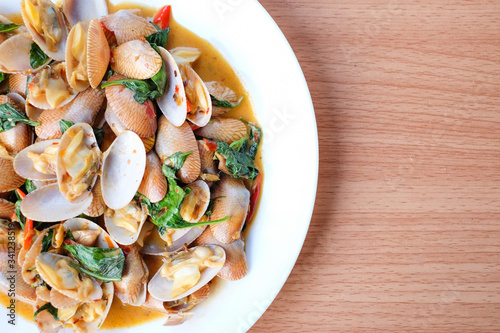 The hot stir fried clams with roasted chili paste and basil serve on white dish set on brown table - homemade food concept.