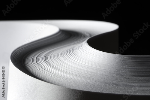 Multiple sheets of rolled A4 paper stack (S-shaped ream) on a black background. Simple, isolated object  with copy space perfect for illustrating various concepts/ideas. Selective focus (shallow DOF).