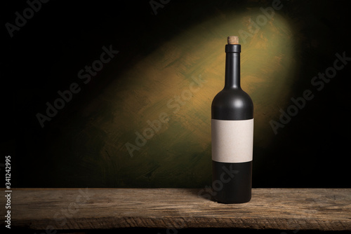 Bartender or male cavist standing near the shelves of wine bottles holds a glass of wine, looks at tint and smells flavor of wine in glass.