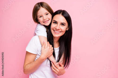 Photo of pretty young mommy hold arms hugging little daughter good mood lovely sincere cardiac feelings piggyback wear casual t-shirts jeans isolated pastel pink color background