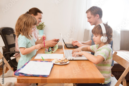 family Mom  dad and two  kids Sitting at the table all together. Children learn onlay from home. work from home with kids. quarantin. Home office.