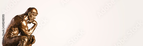 A bronze replica statue of Rodin's Thinker on a white background