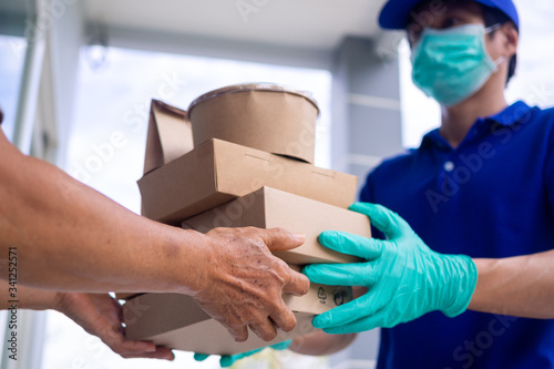 The shipper wears a mask and gloves, delivering food to the home of the online buyer. stay at home reduce the spread of the covid-19 virus. The sender has a service to deliver products or food quickly © Shisu_ka