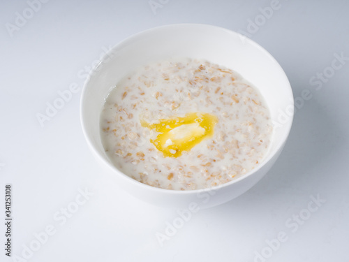 Oatmeal in milk with butter in a white round bowl on a light background. Side view