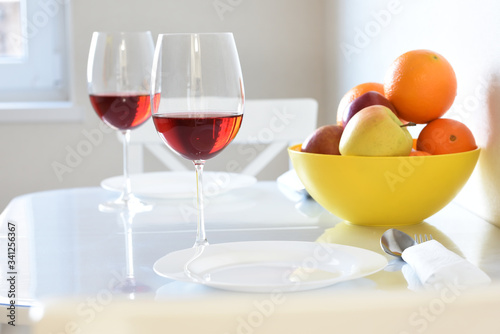 Fruit oranges and apples in a bowl and glasses with wine in a white bright room.