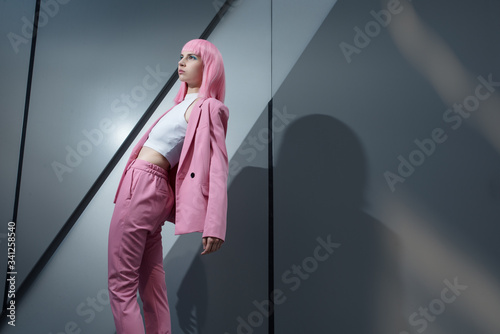 Bilde på lerret Young woman in pink pant suit with pink hair on metallic, business centre wall background