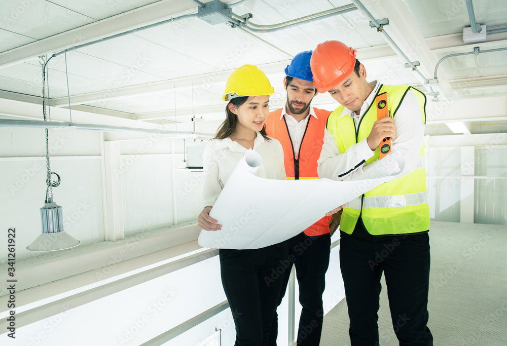 Businessman or engineer architect mixed race young caucasian man and asian woman wear hard hat talking to architects at construction site hand holding blueprint. Businessman or engineer architect mixed race young caucasian man and asian woman wear hard hat talking to architects at construction site hand holding blueprint.