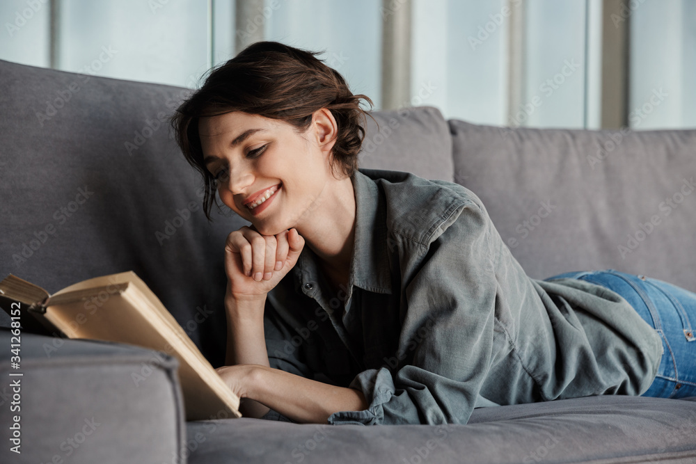 Image of brunette cute pleased woman reading book and smiling Image of brunette cute pleased woman reading book and smiling