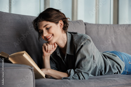 Image of brunette cute pleased woman reading book and smiling