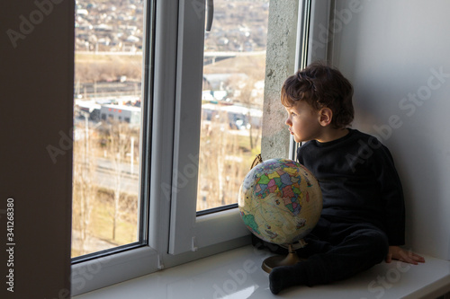 stay positive at home. The child sits on the windowsill and plays with the globe during the worldwide quarantine of the coronavirus pandemic.