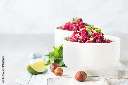 White ceramic bowls with warm buckwheat, beetroot, nuts and herbs salad on wooden board, light grey concrete background. Dietary balanced food. Vegetarian and vegan concept. 
