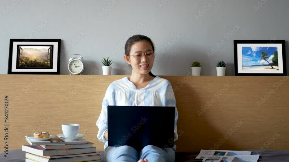 attractive happy woman using video call, make online conversation via laptop computer on bed in her room, having video chat, waving hand with visual screen of conversation partner during self isolated