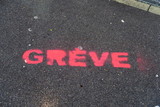 Inscription GREVE peinte à la peinture rose sur le sol de goudron noir dans la rue.