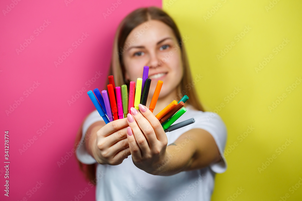 Beautiful young girl in a white T-shirt holds multicolored felt-tip pens for drawing Beautiful young girl in a white T-shirt holds multicolored felt-tip pens for drawing