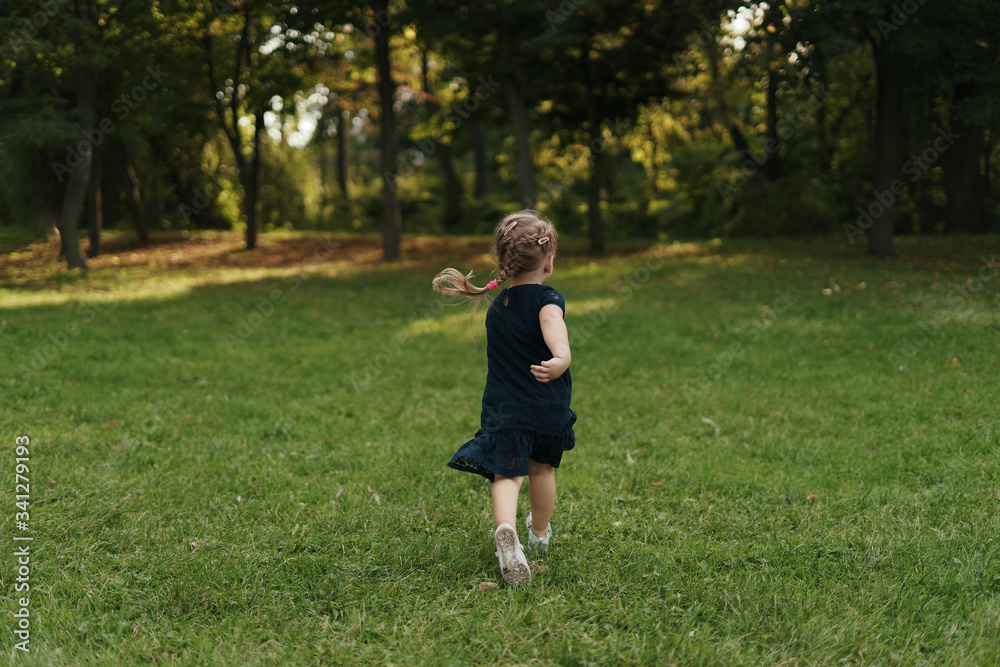 Little cheerful blonde girl wearing a navy dress running in the grass, enjoying life