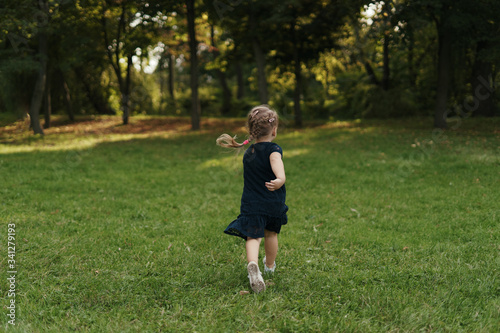 Little cheerful blonde girl wearing a navy dress running in the grass, enjoying life