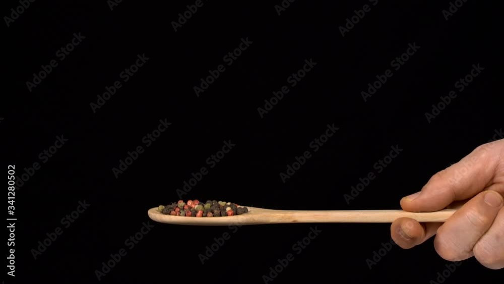 Hands holding a spoon. Different pepper in wooden spoon. Pepper is falling down in slow motion. Nobody in the frame.