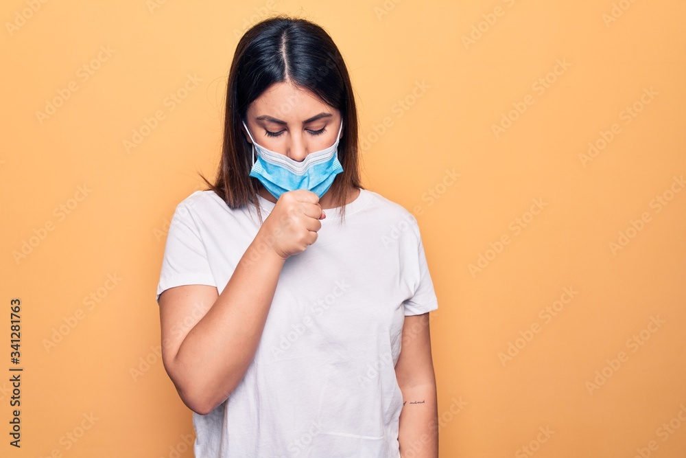Young woman wearing protection mask for coronavirus disease over yellow background feeling unwell and coughing as symptom for cold or bronchitis. Health care concept. Young woman wearing protection mask for coronavirus disease over yellow background feeling unwell and coughing as symptom for cold or bronchitis. Health care concept.