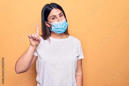 Young woman wearing protection mask for coronavirus disease over yellow background smiling with an idea or question pointing finger up with happy face  number one