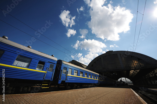 Beautiful train with blue wagons at the railway station at sunset. Industrial view with modern train, railroad, railway platform, buildings, cloudy sky