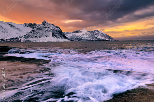 View over Ersfjord from colorful rocks at sunset and rockpools to snowy mountains on a dark cloudy day, Cape Tungeneset, Senja, Norway. Europe. Long exposure shot
