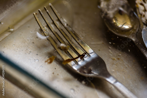 dirty fork knife and spoon covered with icing under water inside kitchen sink