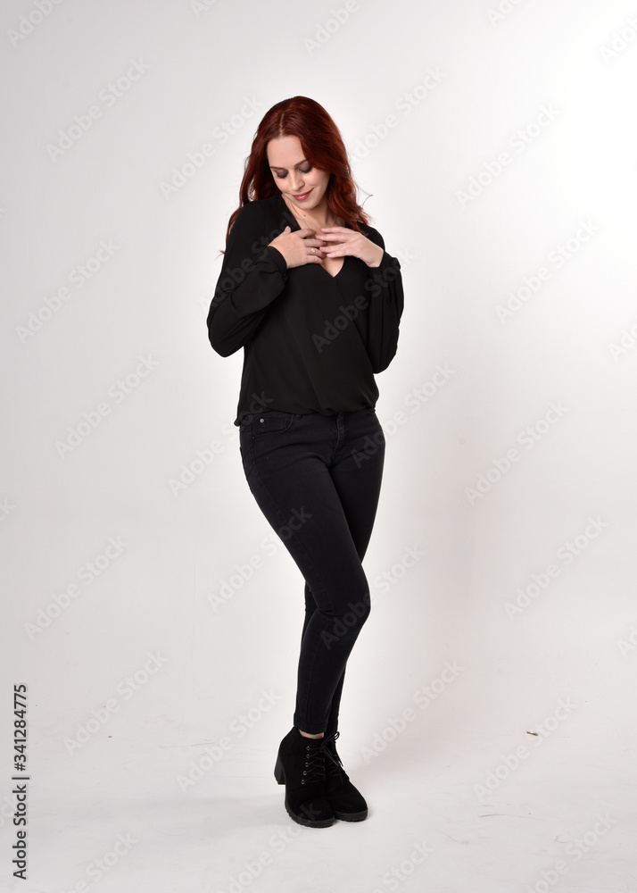 Portrait of a pretty girl with red hair wearing black jeans, boots and a blouse. full length standing pose, facing the camera, on a studio background. Portrait of a pretty girl with red hair wearing black jeans, boots and a blouse. full length standing pose, facing the camera, on a studio background.