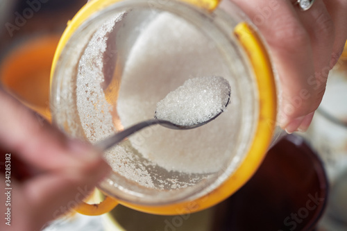 A female hand takes a teaspoon of sugar from a can. Close-up
