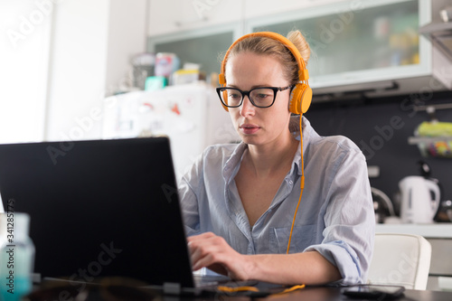 Female freelancer in her casual home clothing working remotly from her dining table in the morning. Home kitchen in the background. Stay healthy and stay at home during corona virus pandemic. photo