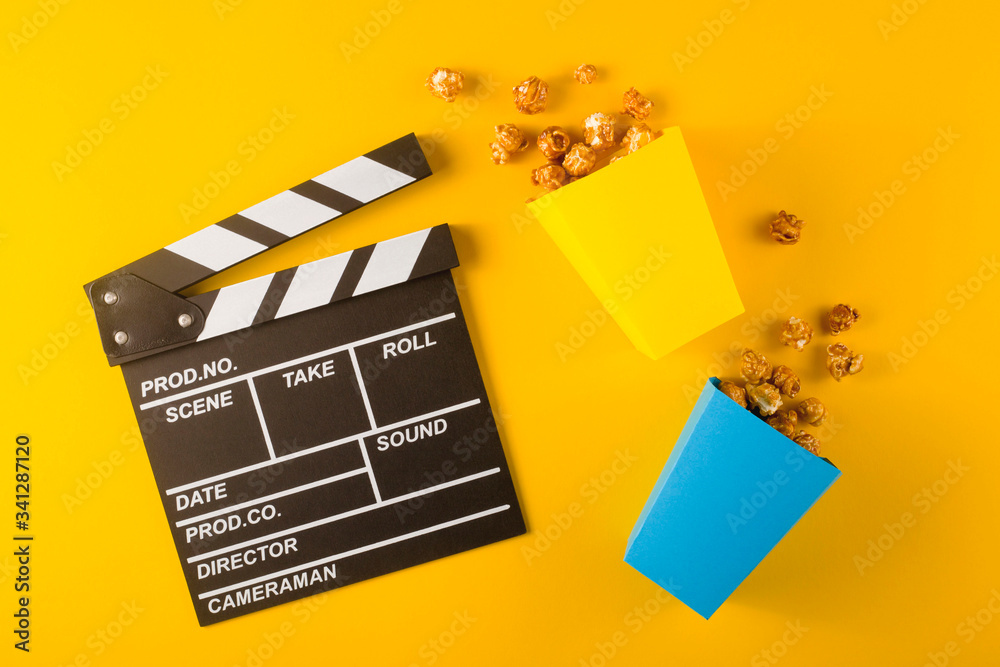 Clapperboard with two boxes of caramel popcorn on yellow background. Top view, flat lay.
