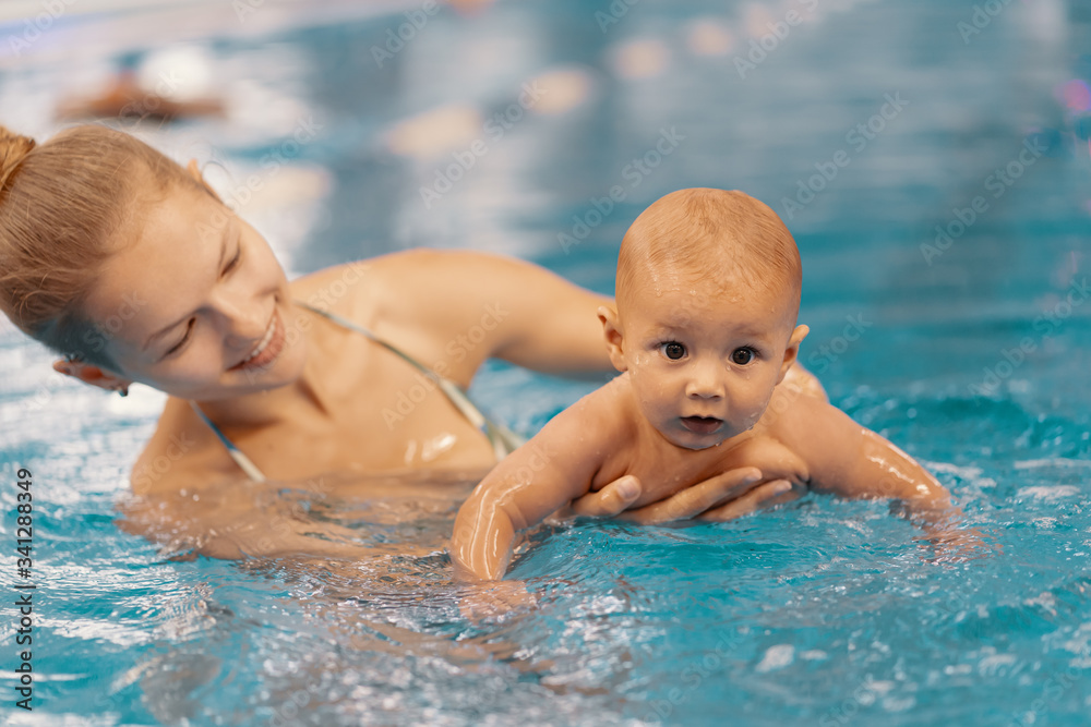Young mother and her baby enjoying a baby swimming lesson in the pool. Child having fun in water with mom Young mother and her baby enjoying a baby swimming lesson in the pool. Child having fun in water with mom