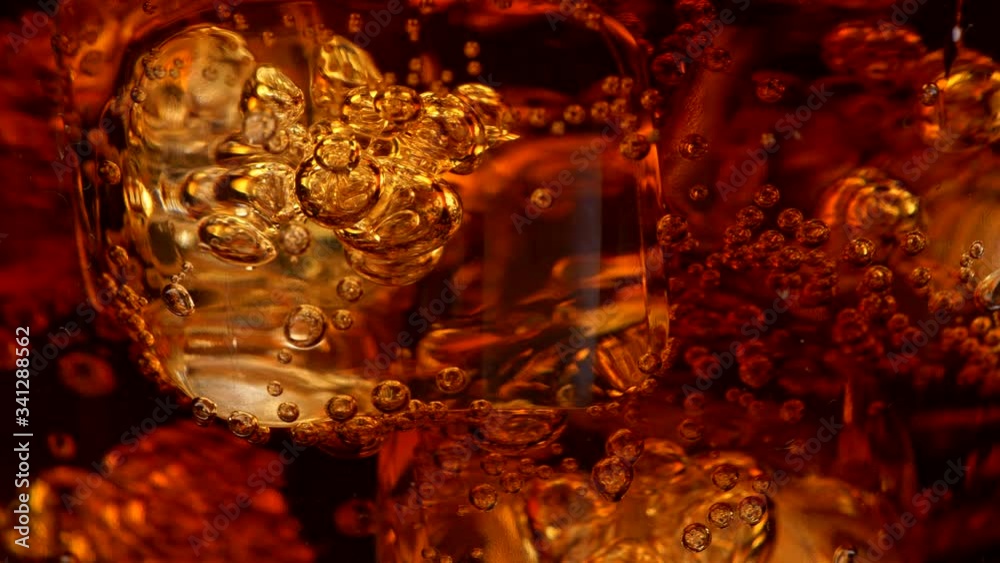 Ice cubes with bubbles in a rotating glass of cola. Abstract super close-up shot, UHD