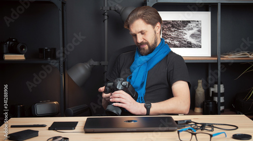 Front view of pleased photographer reviewing taken shots in DSLR camera sitting at table in studio