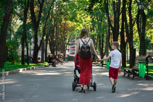 Mom walks in the Park with stroller and elder son. Walk with children. Childhood Lifestyle