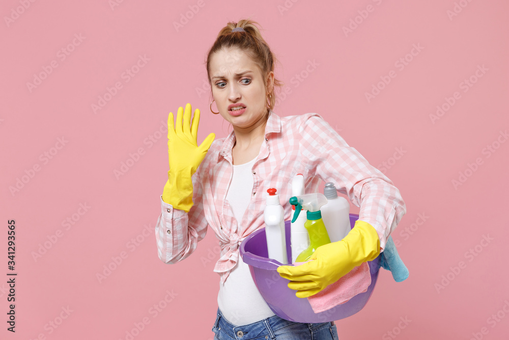 Disgusted young woman housewife in rubber gloves hold basin with detergent bottles washing cleansers doing housework isolated on pink background. Housekeeping concept. Showing stop gesture with palm. Disgusted young woman housewife in rubber gloves hold basin with detergent bottles washing cleansers doing housework isolated on pink background. Housekeeping concept. Showing stop gesture with palm.