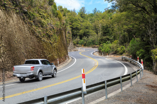 A scenic, winding road in the New Zealand hills, with a cliff on one side and native forest on the other photo