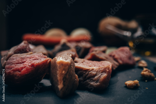 Pieces of raw meat on a black board with various ingredients in an unfocused background. Copy space.Concept of dark food