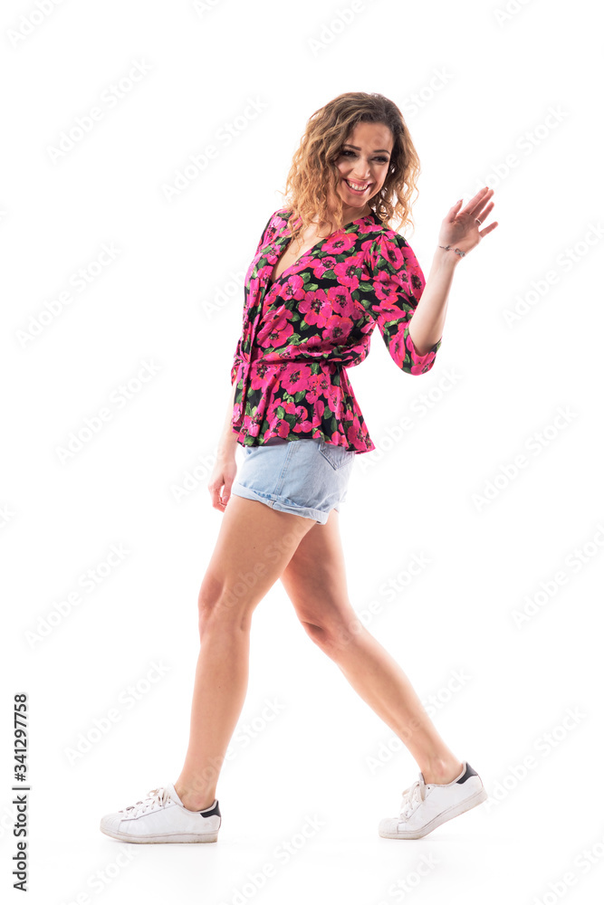 Naklejka premium Side view of cheerful young stylish woman walking away turning back and waving hand goodbye. Full body isolated on white background. 